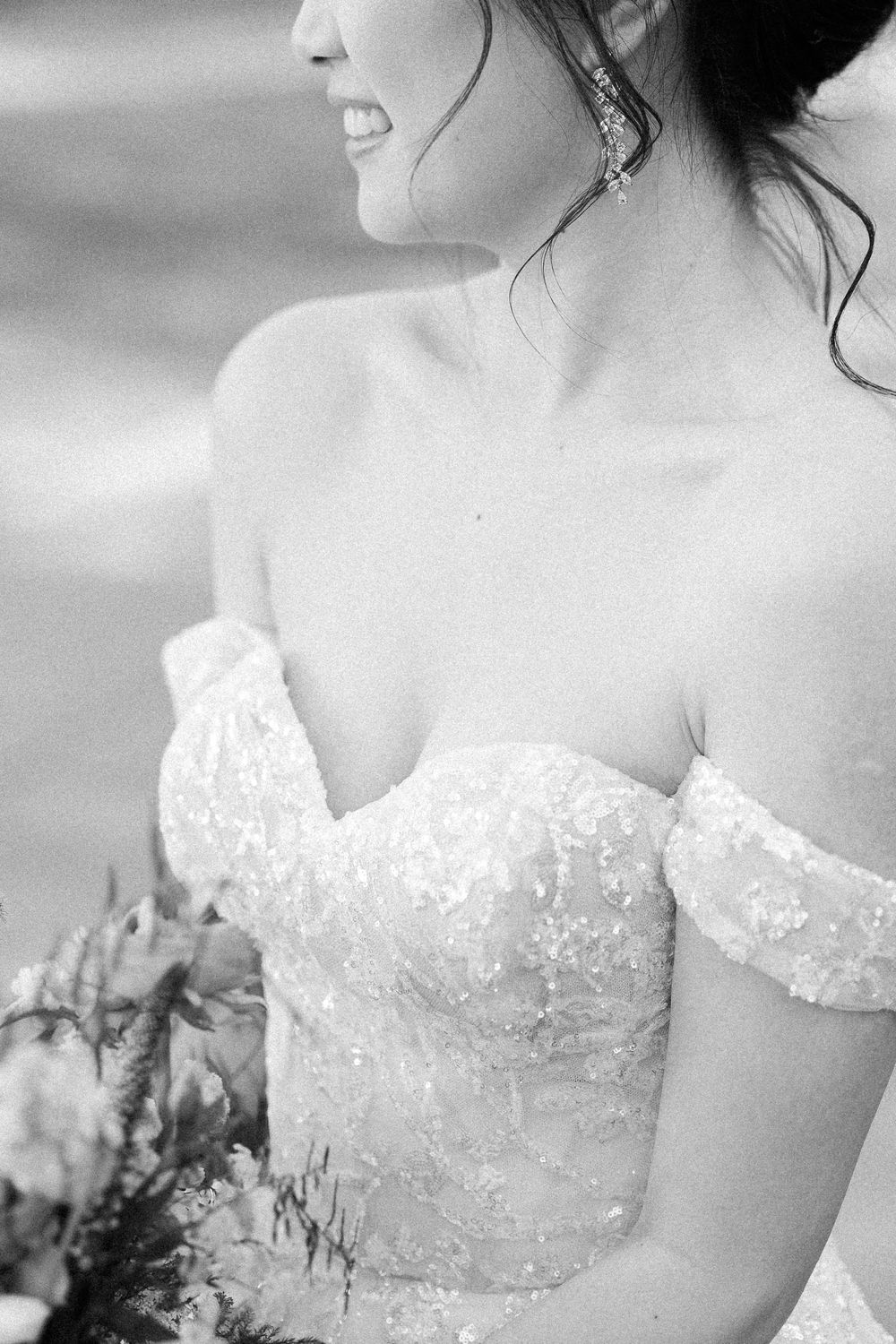 Close up of delicate off-shoulder lace wedding dress bodice in black and white photography.