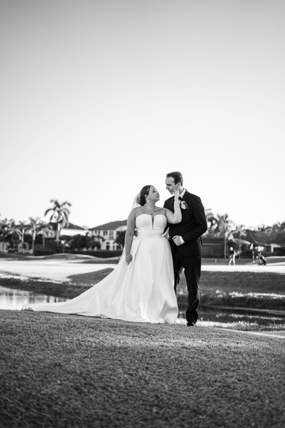 Black and white photo of a bride and groom walking together on a golf course, smiling at each other on their wedding day.