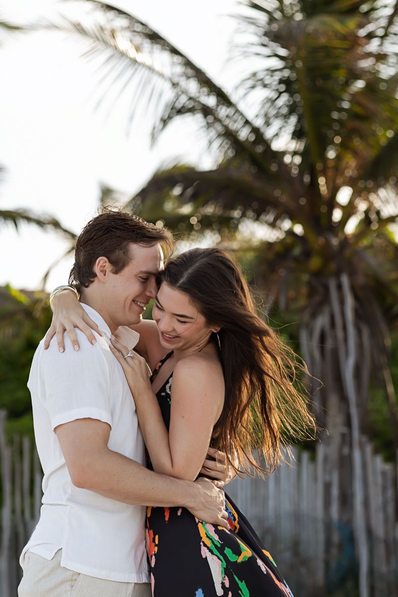Happy couple embraces and laughs together near palm trees on a beach.