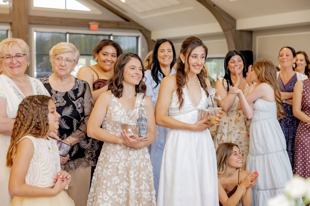 Brides surrounded by smiling guests during wedding celebration indoors.