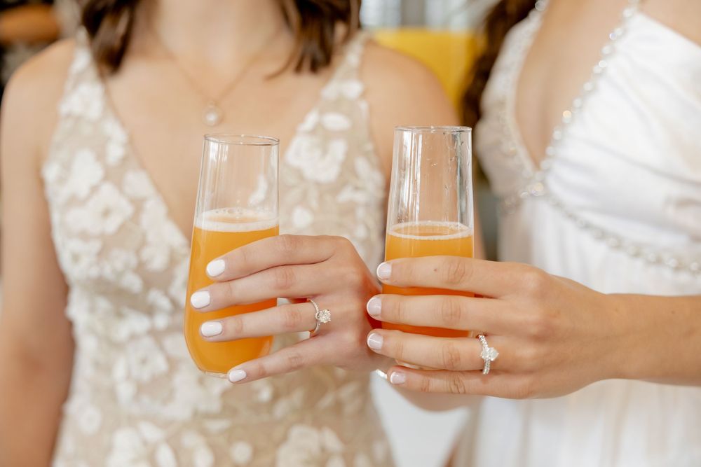 Two brides in white dresses toasting with mimosas juice at a wedding celebration.