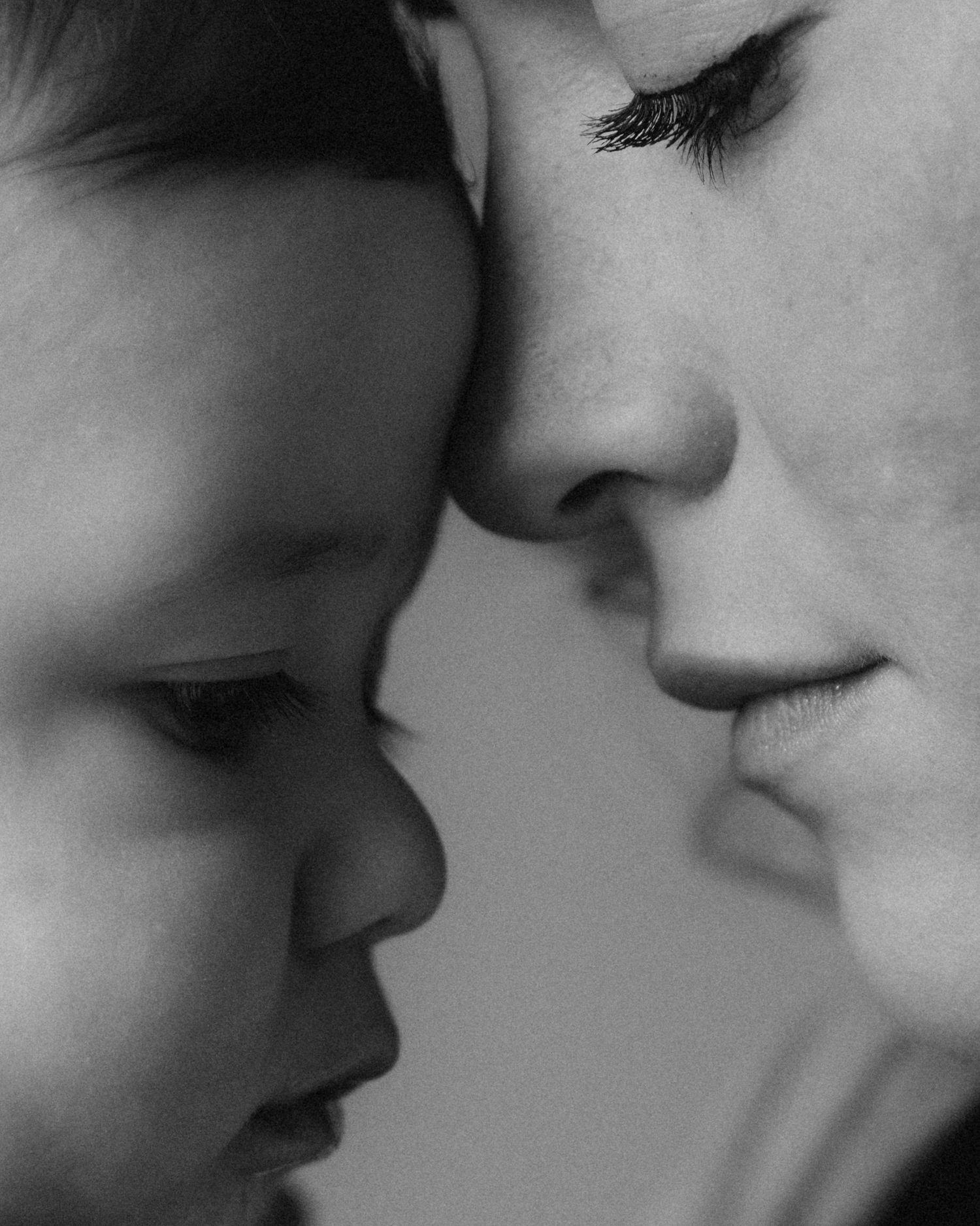 Black and white close-up of a mother and young child touching foreheads in a tender, loving moment.
