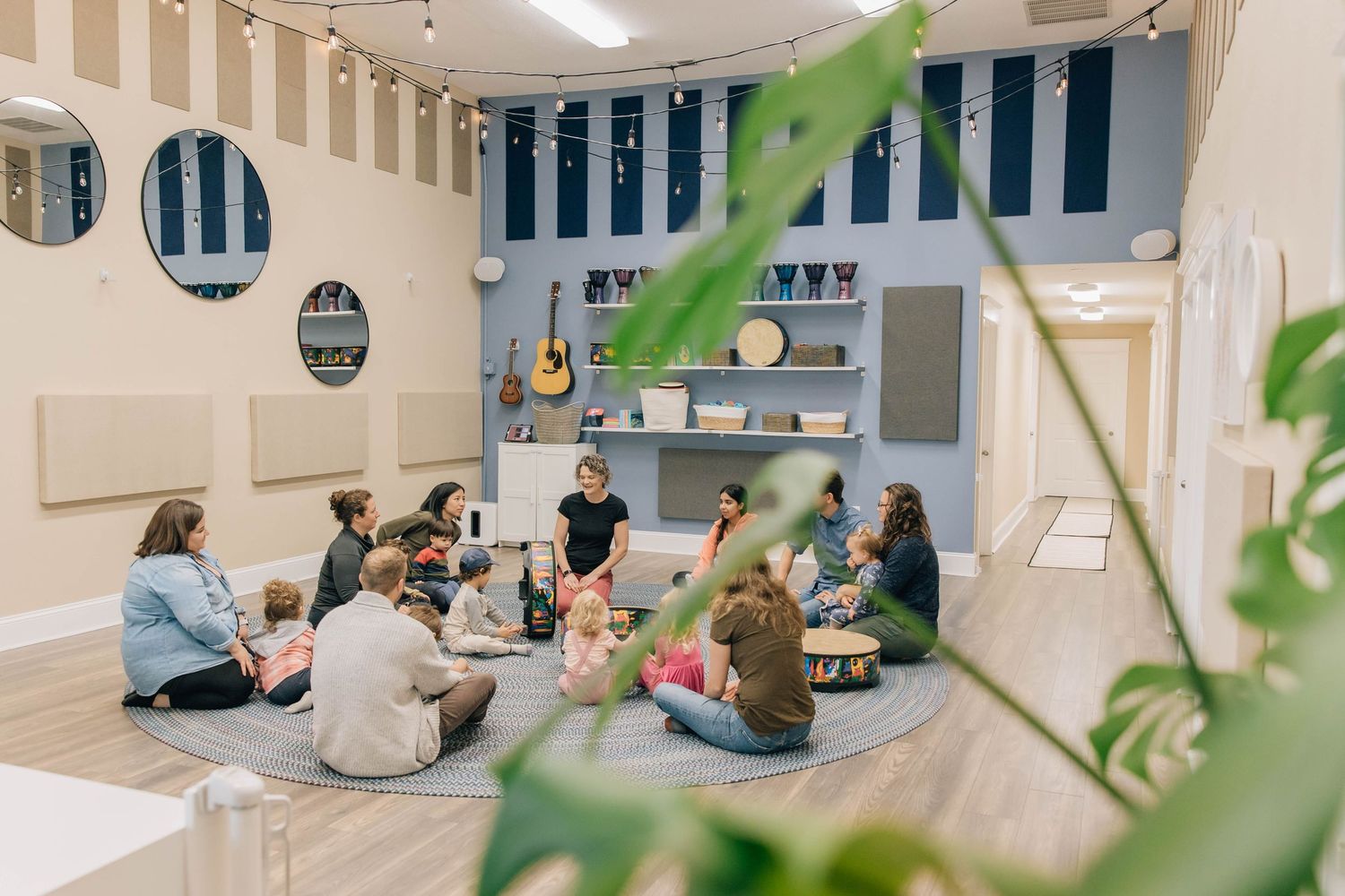 Group of parents and toddlers sitting in circle during music class in bright modern studio.