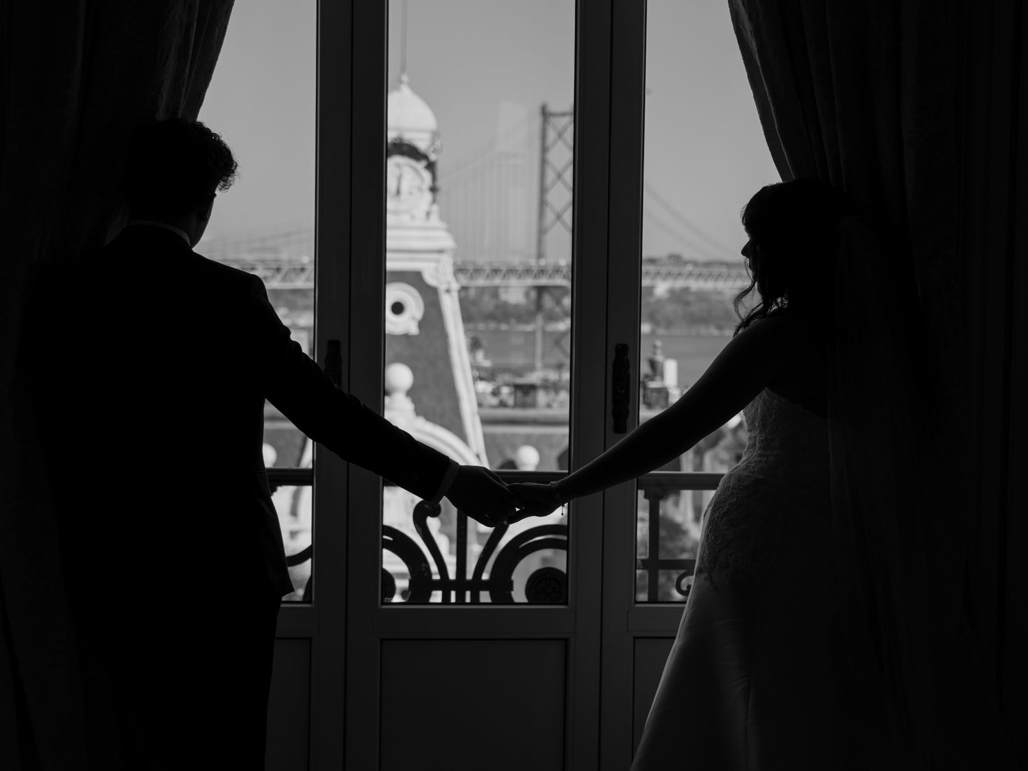 A couple embraces outdoors against a green hedge wall, with the bride wearing an elegant lace off-shoulder wedding gown.