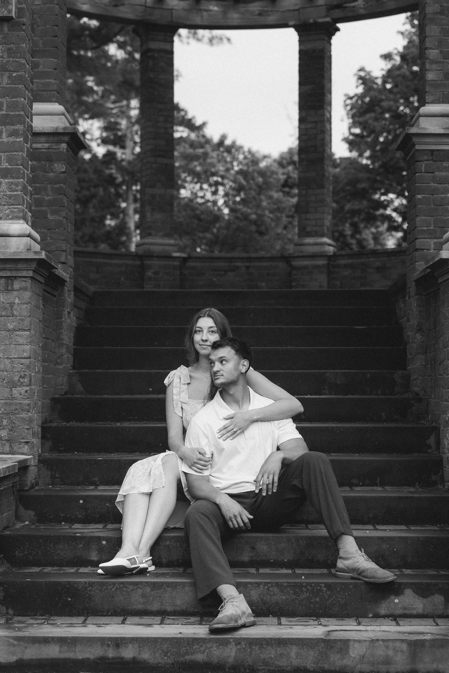Black and white photo of a romantic couple sitting together on stone steps near classical columns.