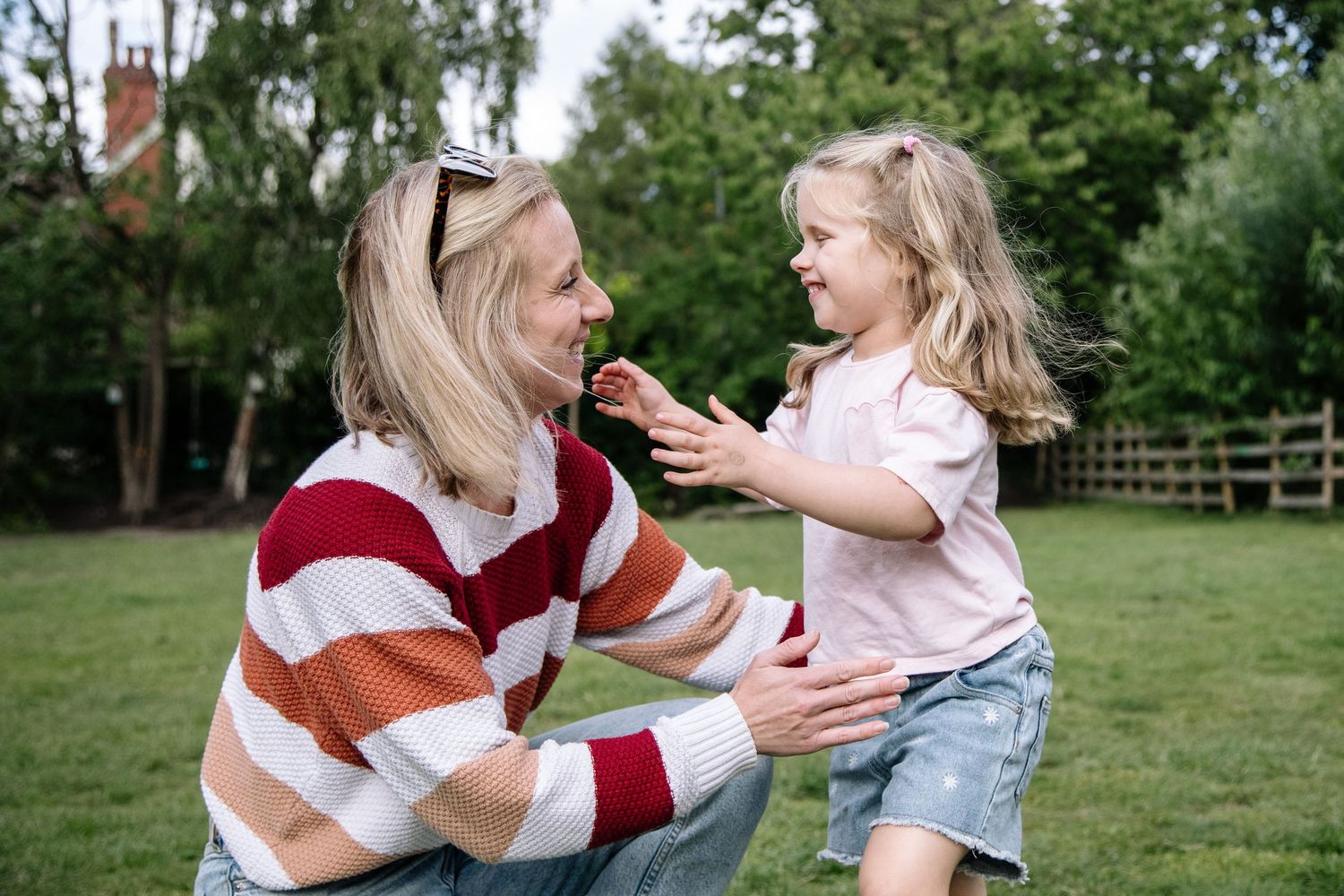 Woman kneeling in garden sharing a strawberry with a smiling young girl on a sunny day.
