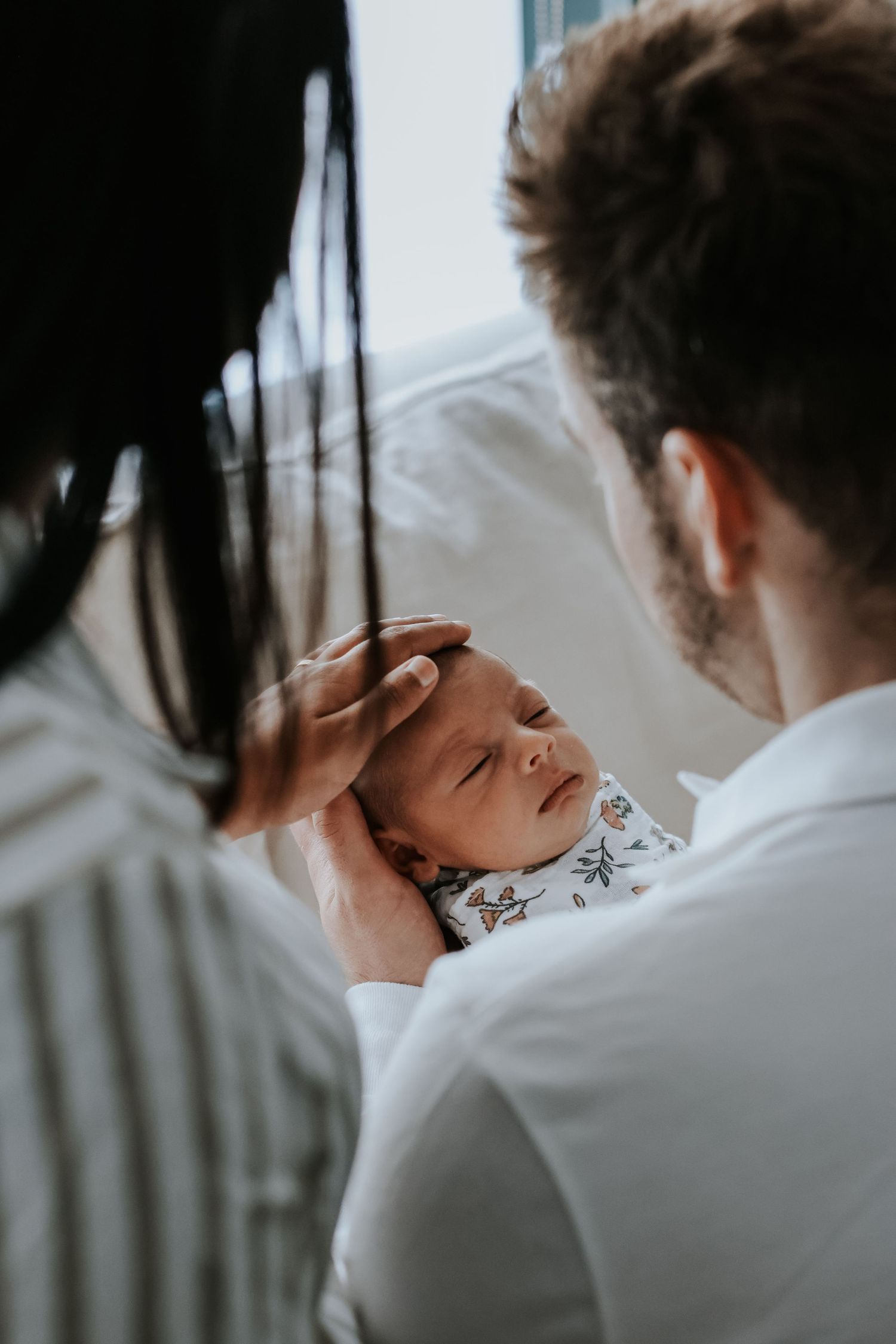 Parents lovingly cradling their newborn baby, with mother gently stroking infant's head in a tender family moment.