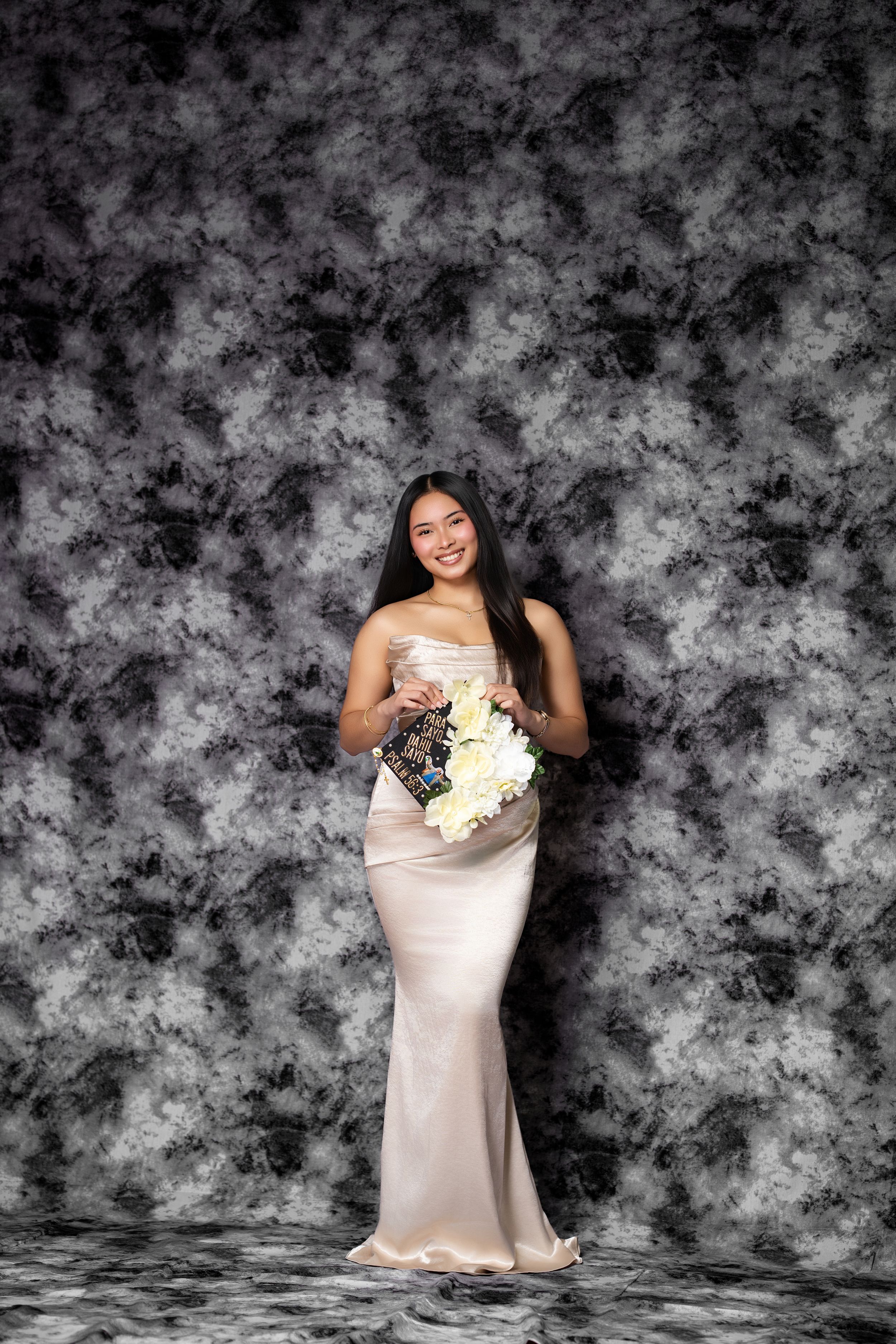 Elegant woman in strapless champagne gown holds white floral bouquet against gray marble backdrop.