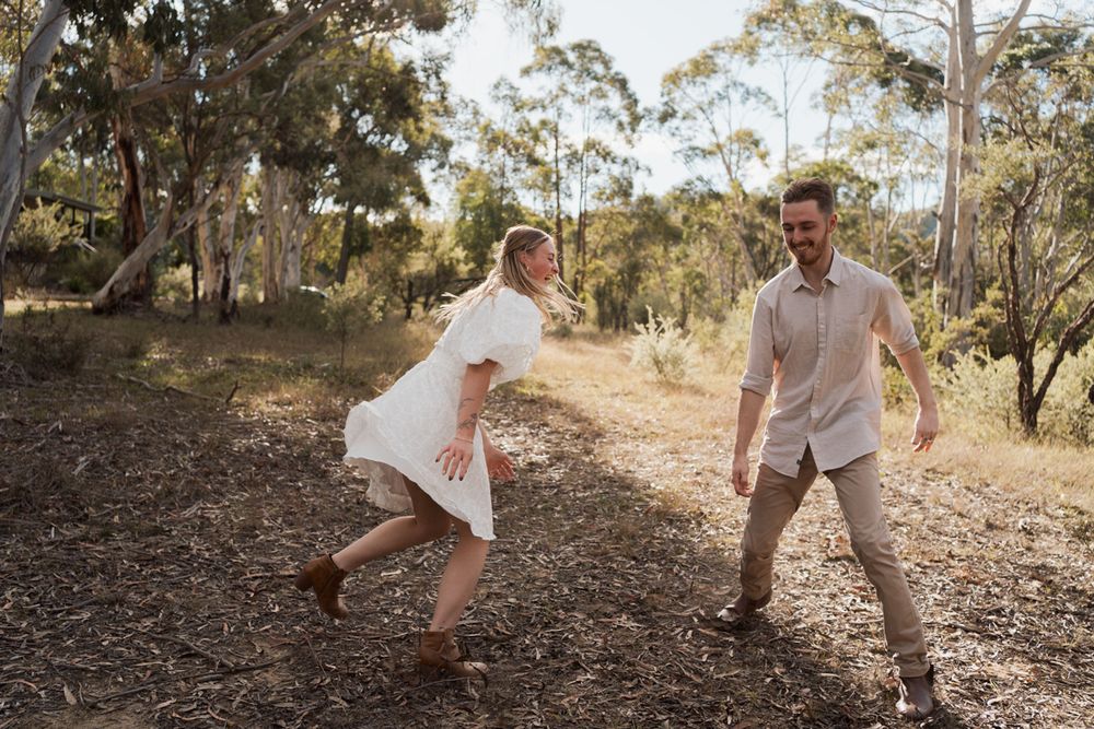 A joyful couple dances playfully on a sunlit bush trail surrounded by eucalyptus trees in Australia. couples photoshoot