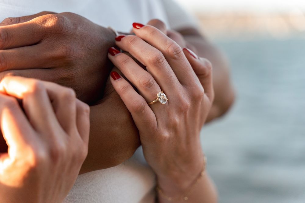 Close-up of hands embracing, featuring a gold diamond engagement ring on a woman with red nail polish. Proposal photoshoot in sydney