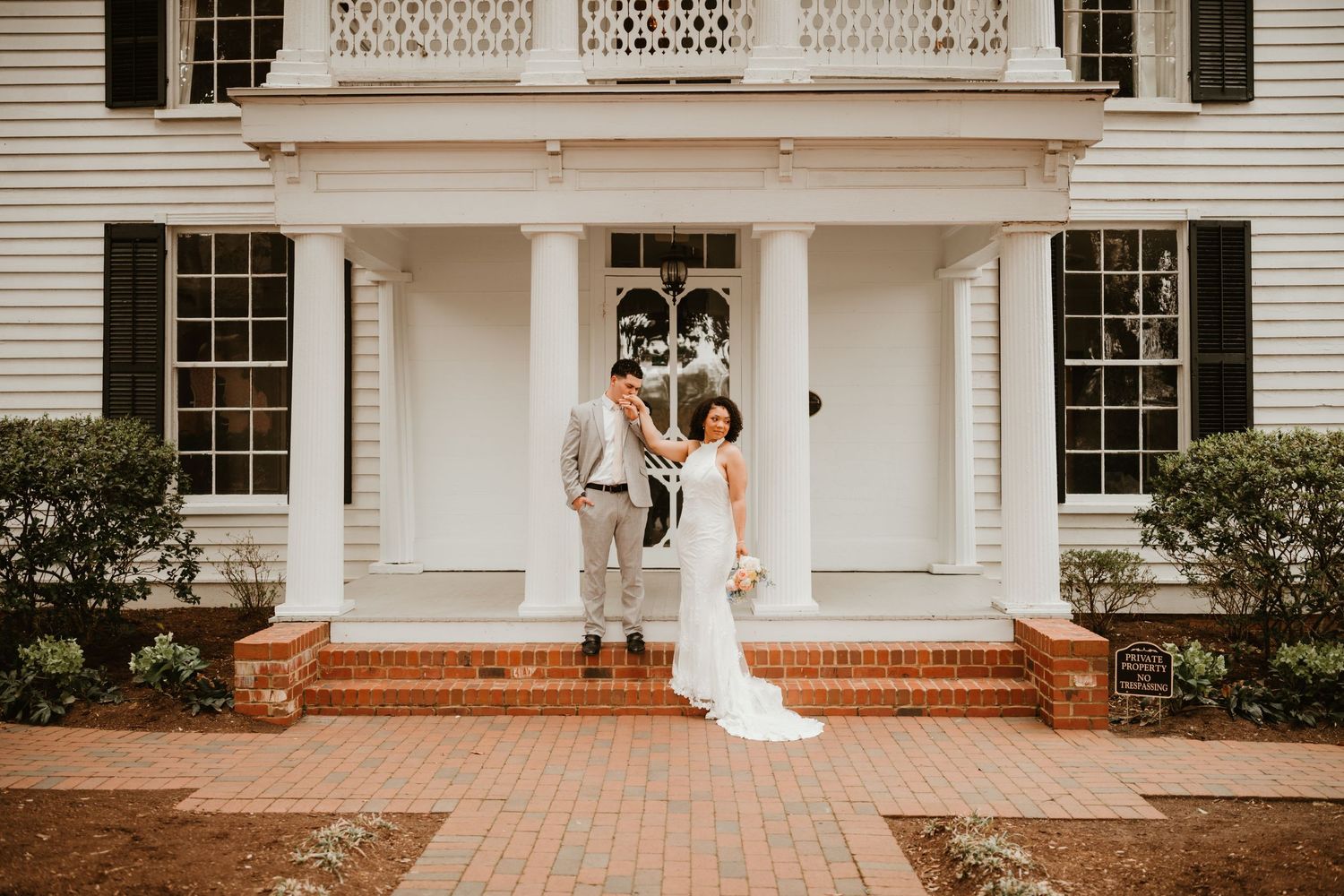 Bride and groom dancing on brick steps of elegant white colonial wedding venue with grand columns. Leslie Alford Mims House venue location.