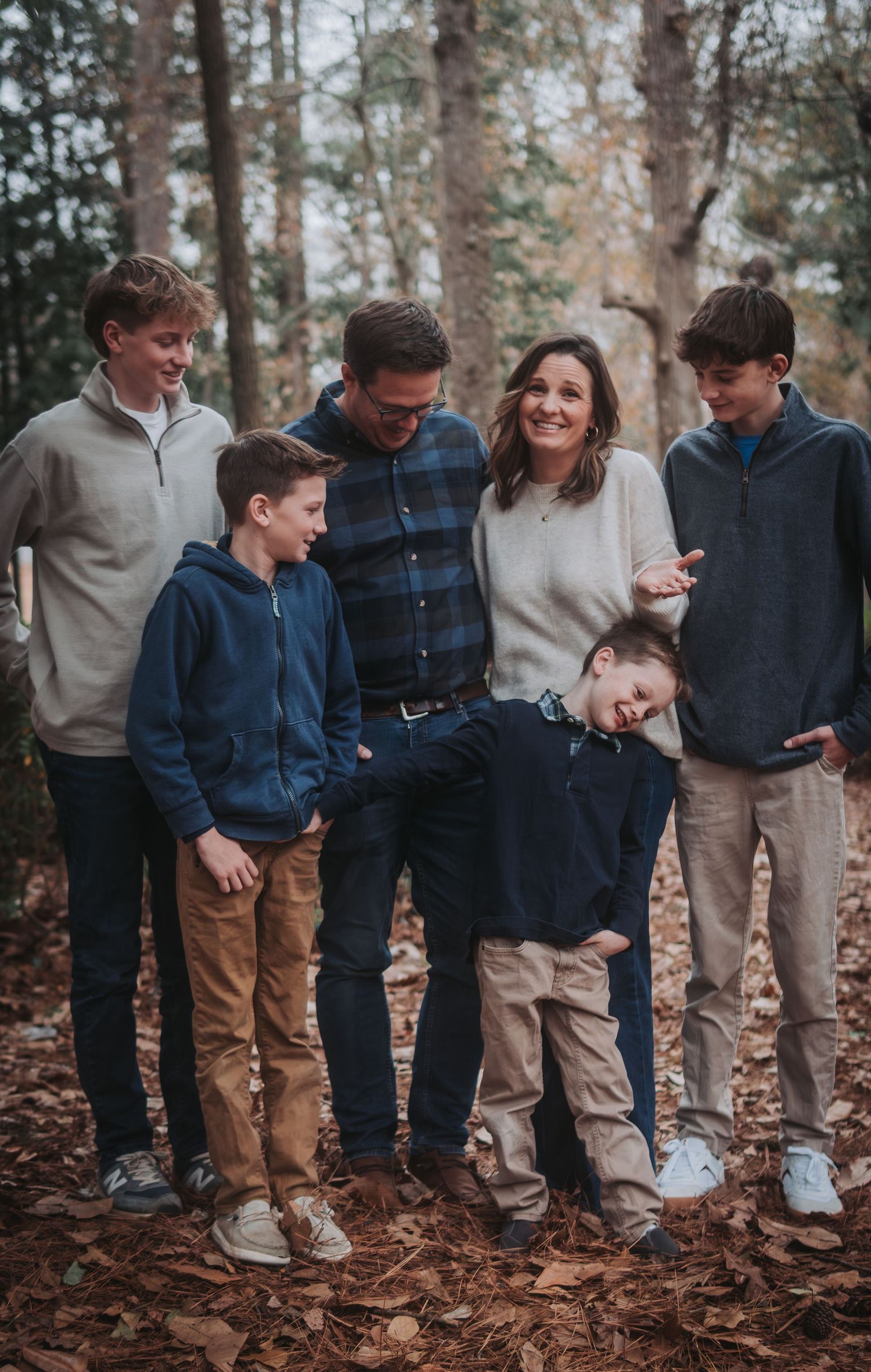 Happy family of six with four boys laughing together in autumn forest setting.