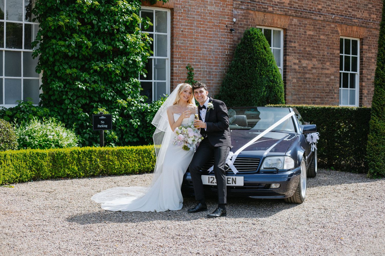 Black and white wedding photo of smiling bride with veil and groom in suit sharing a romantic moment outdoors.