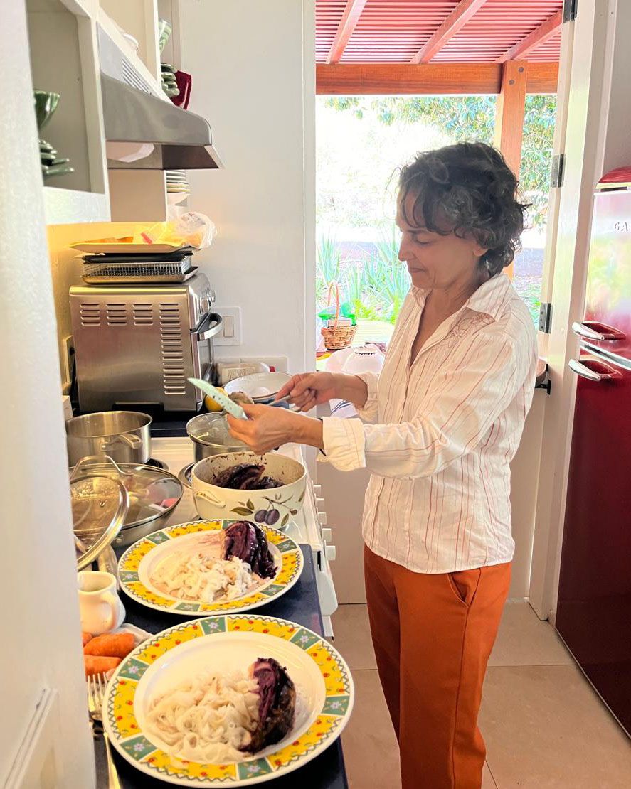 Woman in white shirt and orange pants plating food in a modern kitchen with colorful dishes.
