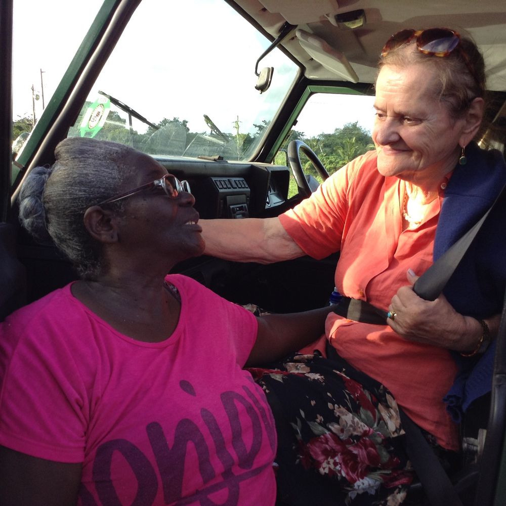 Two elderly women sharing a warm moment inside a vehicle, one in a pink shirt, smiling and connecting.
