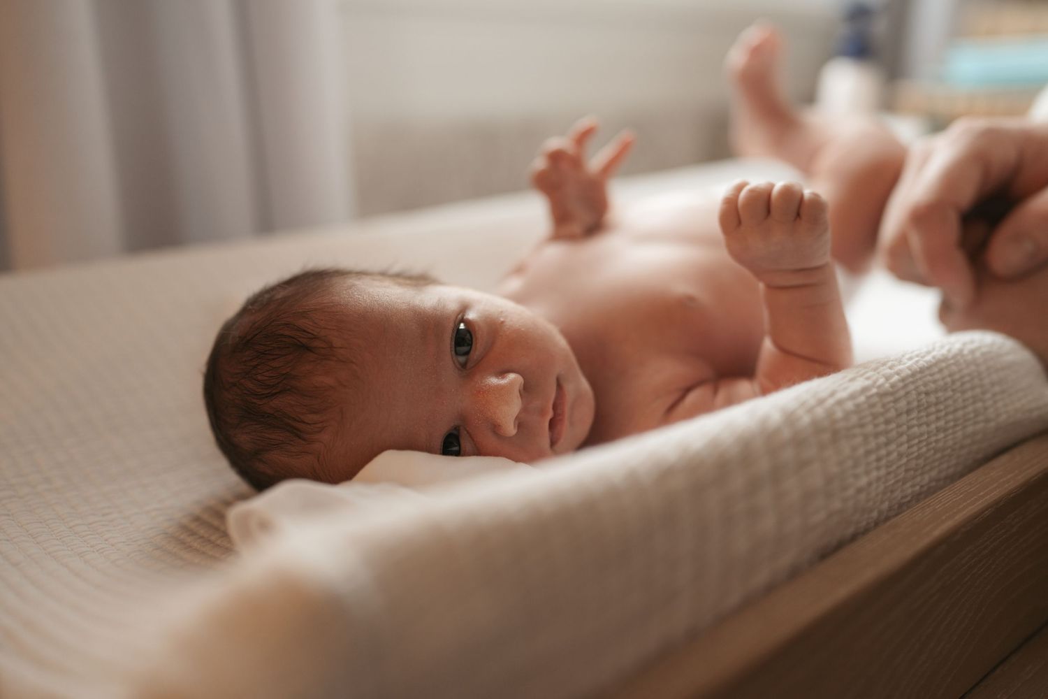 Newborn baby lying on a changing table, looking up with dark eyes, in a softly lit nursery room.