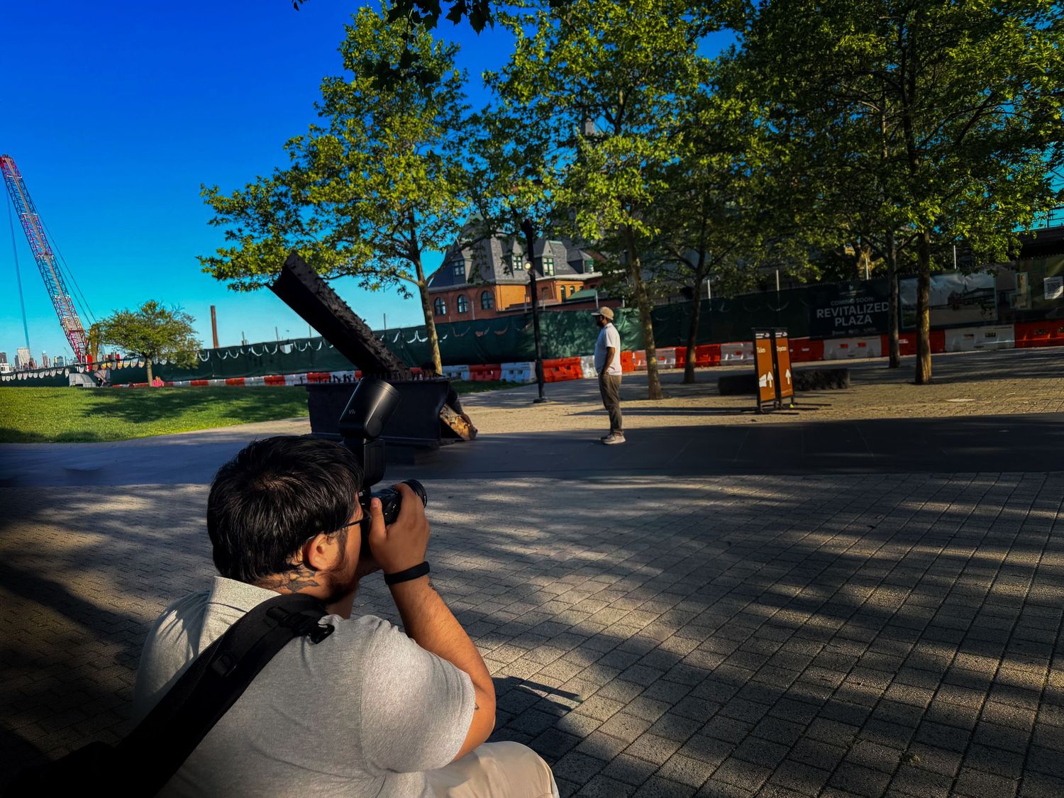 Photographer sitting outdoors capturing photos near a waterfront construction site on a sunny day.