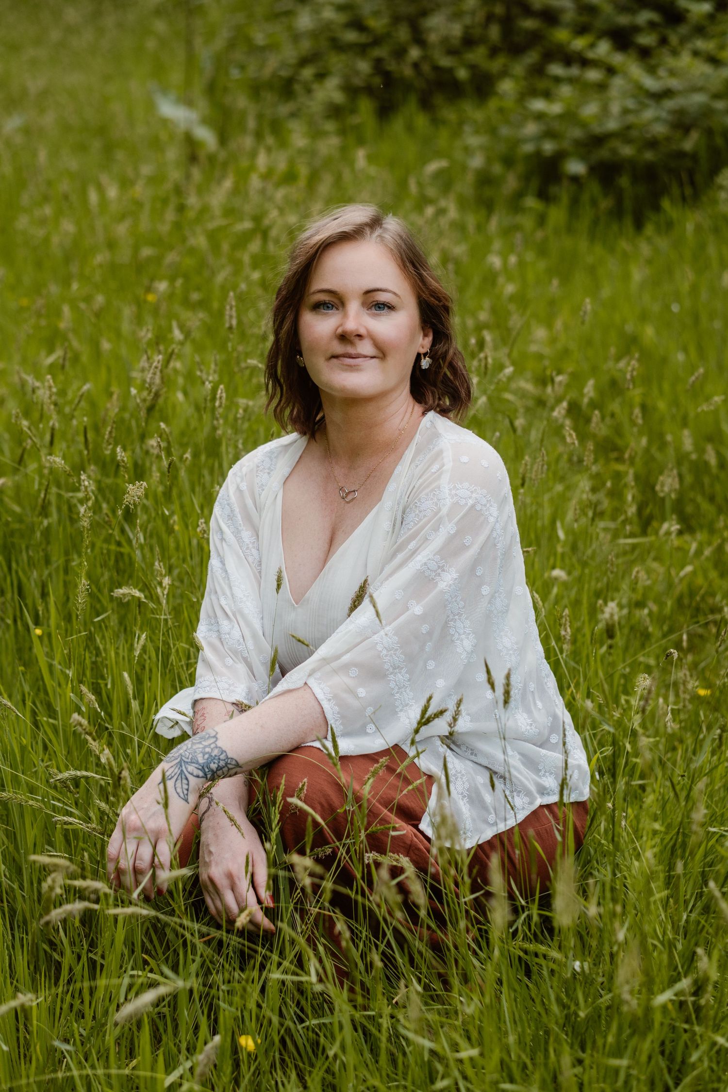 Smiling woman with red hair in green cardigan and jeans sitting on stone steps by a rustic blue door.