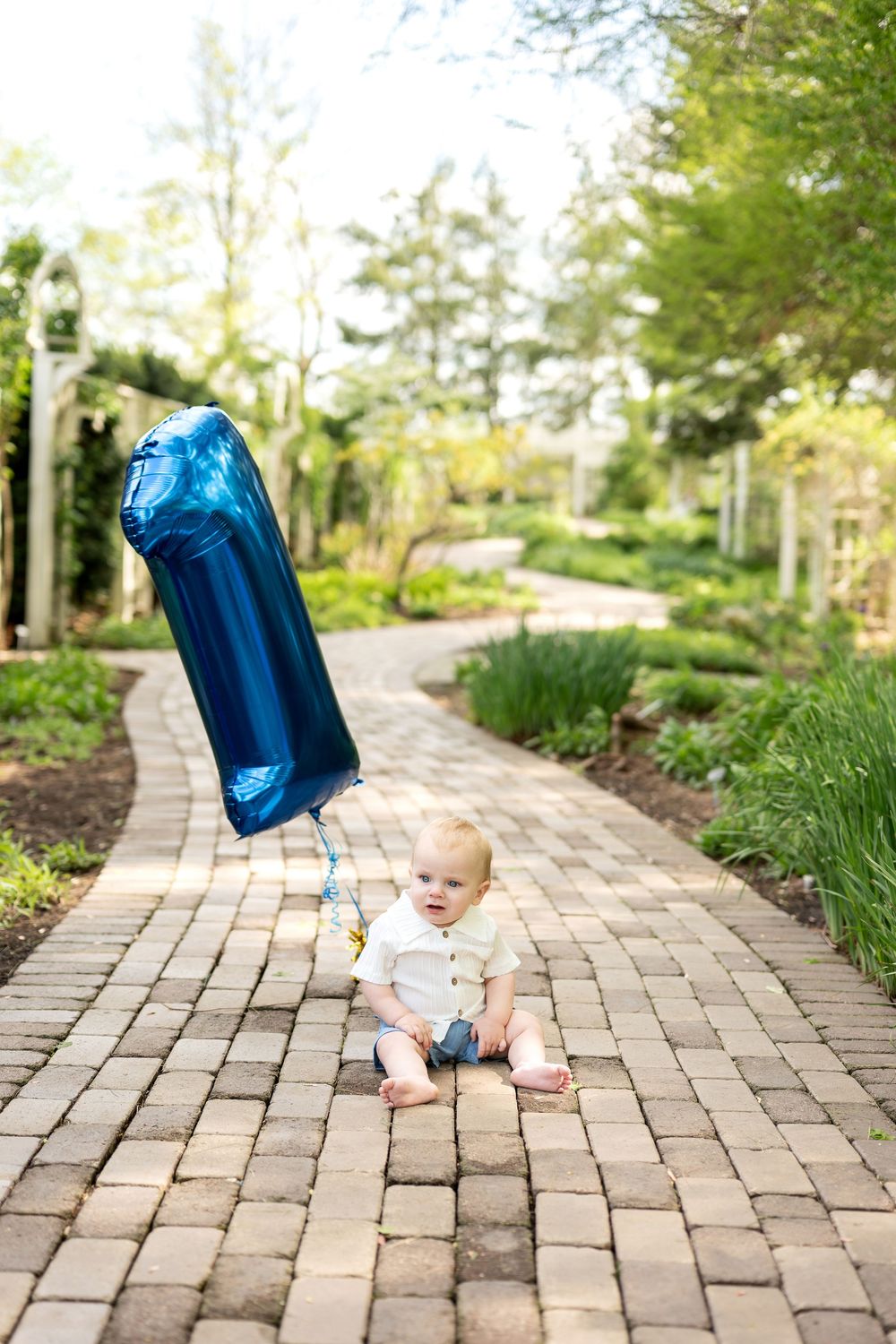Infant on garden brick path with blue number 1 foil balloon.