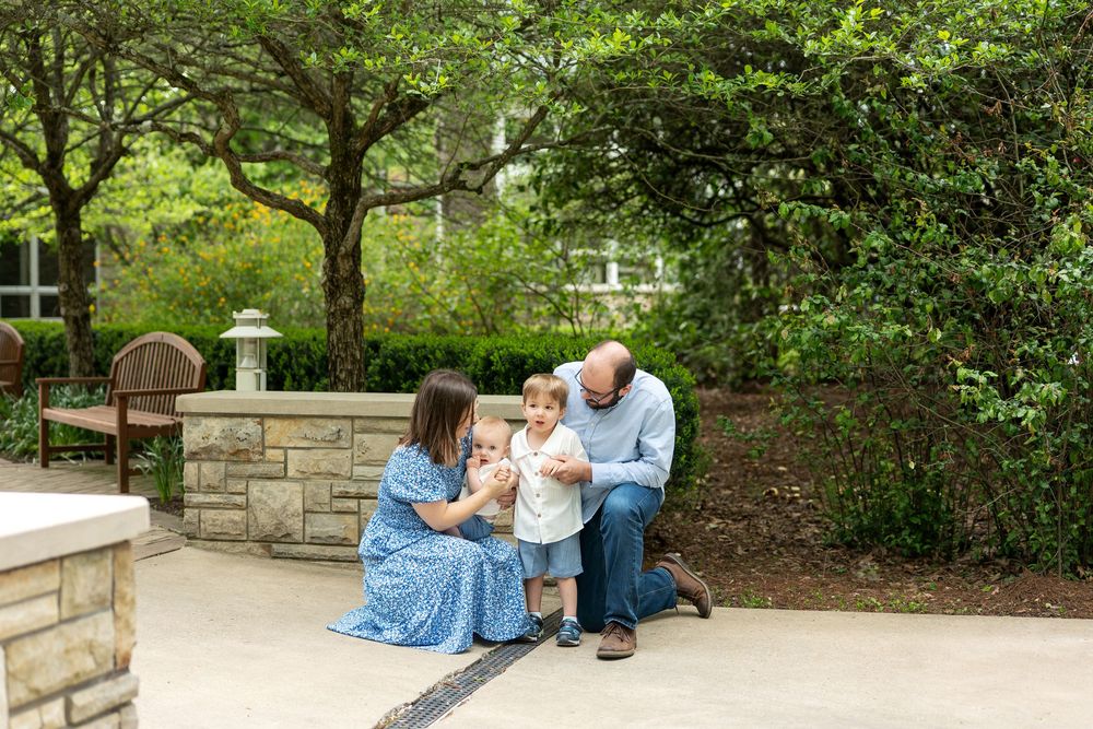 Family with two young children enjoying a sunny day in a lush garden patio setting.