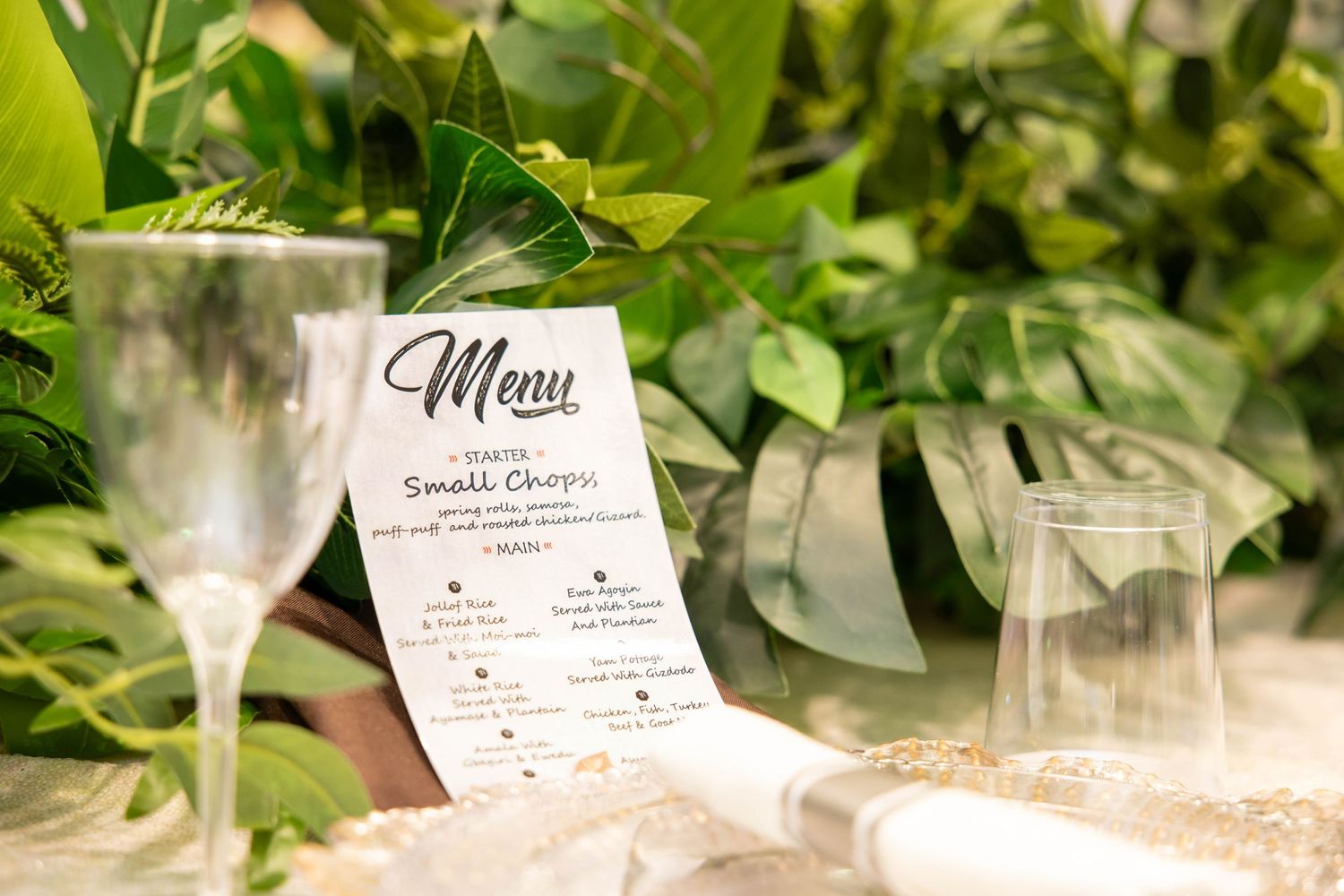 Elegant wedding menu card displayed beside champagne glasses and lush tropical greenery on a decorated table.