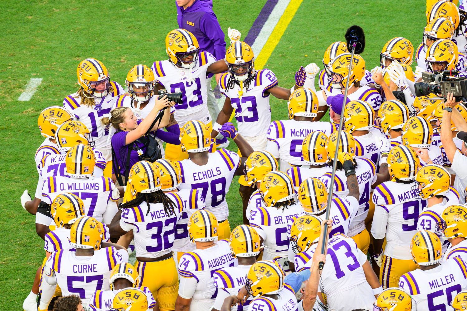 LSU Tigers football team huddles together on the field in purple and gold uniforms during a college football game.