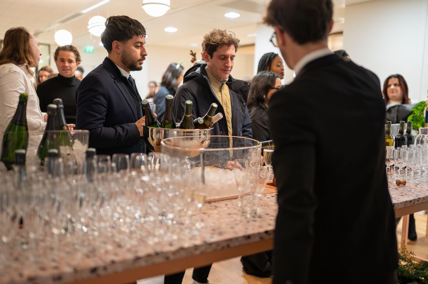 Des barmans servant du champagne lors d'un élégant événement de réception intérieur avec des rangées de verres à vin sur une longue table.