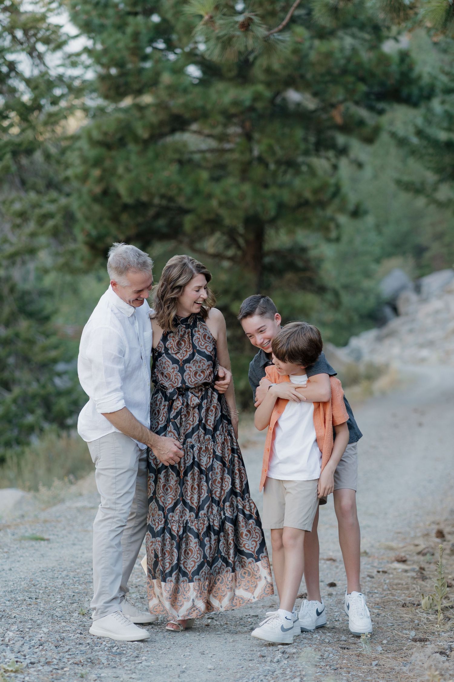 Family enjoying a playful moment together on a rocky mountain trail with pine trees in the background.