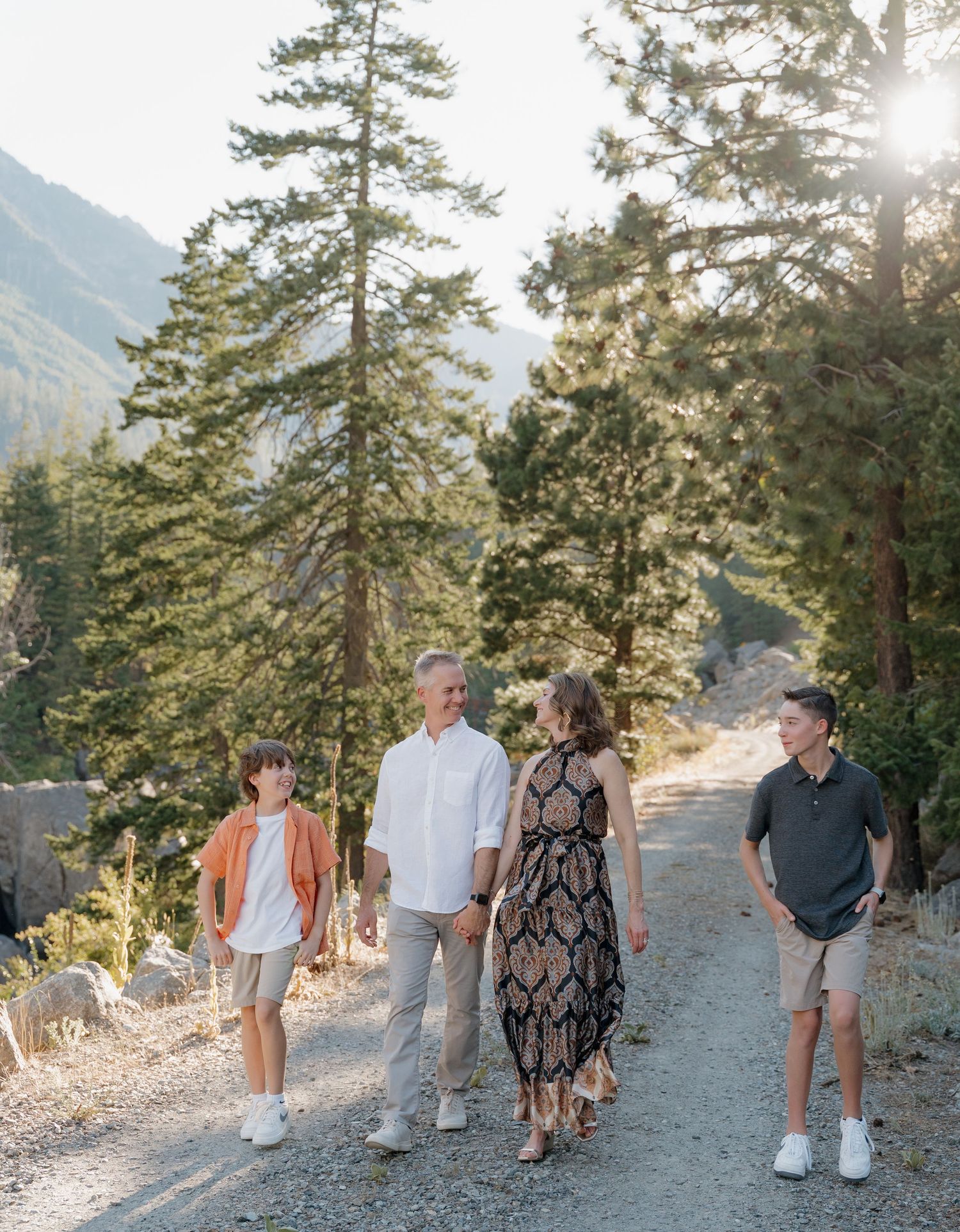 A group walks together on a scenic mountain trail during golden hour with pine trees and sunlight in the background.