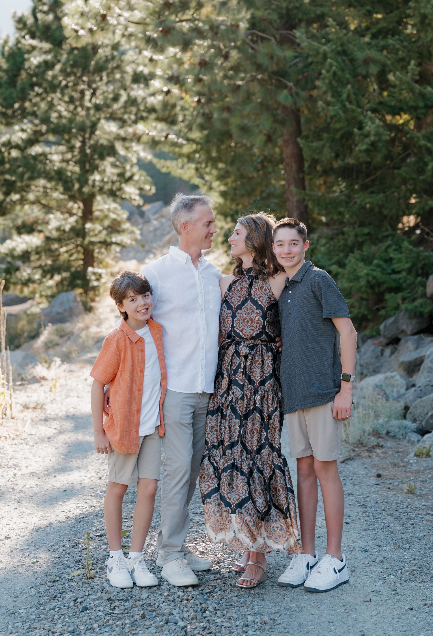 Family group poses together on a scenic mountain path with evergreen trees in the background.