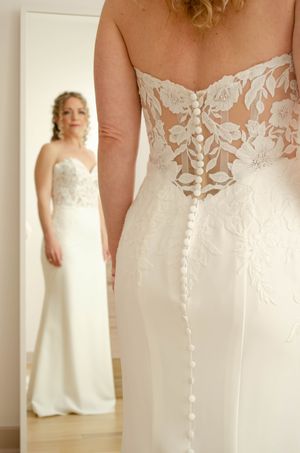 Bride in elegant strapless lace wedding gown with button back detail, reflected in mirror.