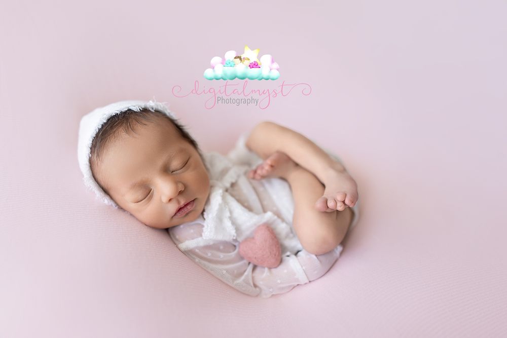 Peaceful newborn baby sleeping on pink backdrop wearing white lace bonnet and wrap in professional photography studio.
