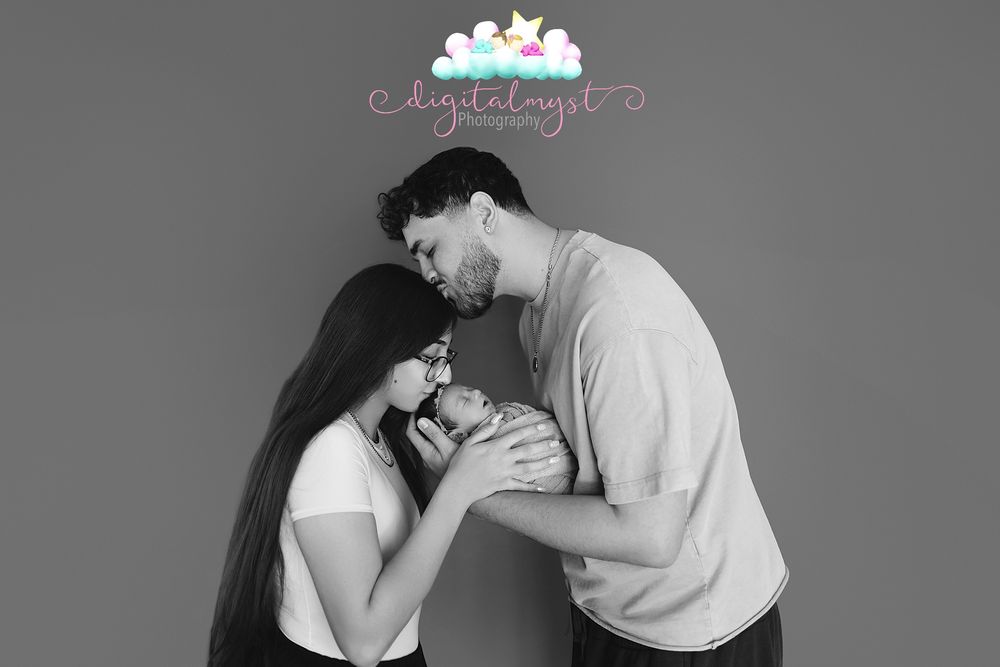 Black and white photo of a couple tenderly kissing their newborn baby, captured by Digitalangel Photography.