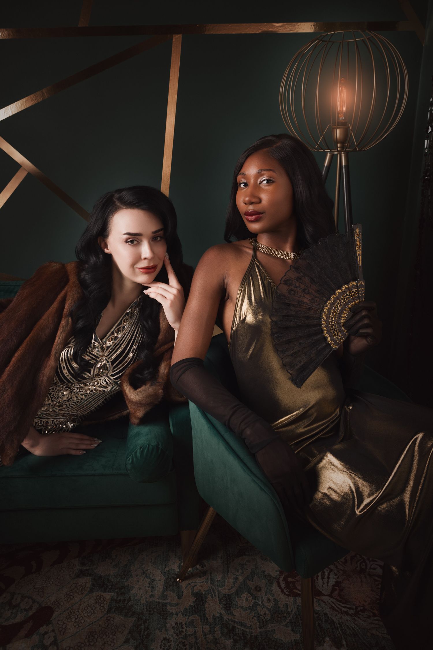 Two elegant women in gold dresses holding cocktail glasses pose for a glamorous portrait against a dark green background.
