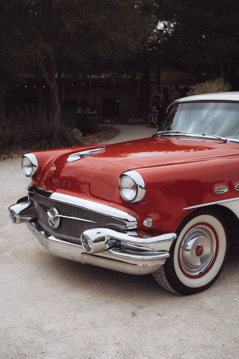 Classic red vintage Buick car with chrome details and whitewall tires parked outdoors at dusk.