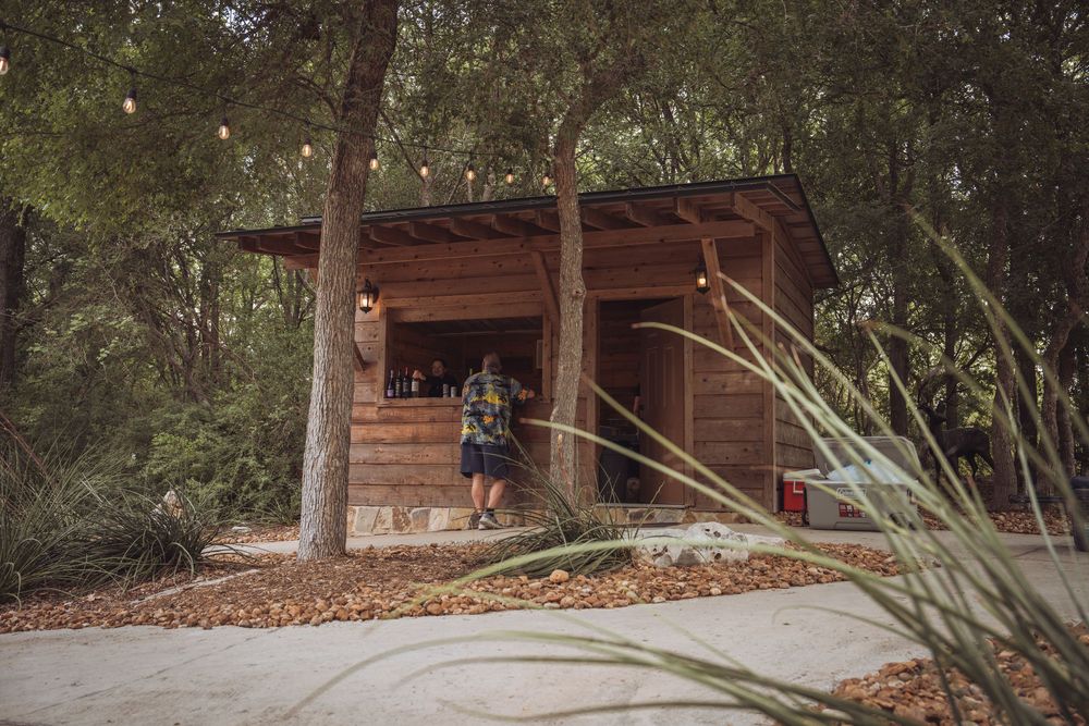 Rustic wooden bar cabin with string lights nestled among trees at an outdoor venue.