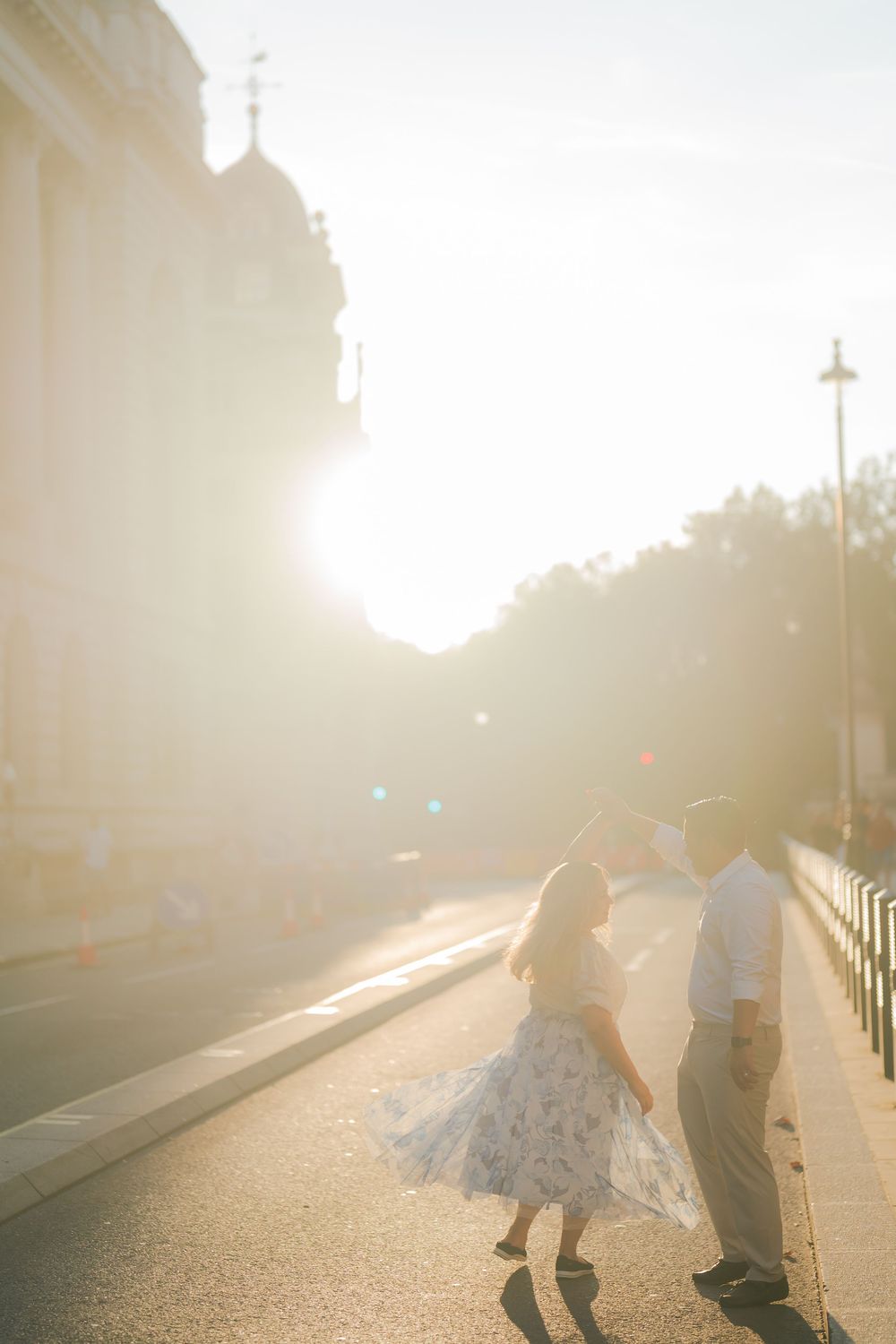 Couple dancing on a sunlit city street at golden hour, with warm lens flare and a flowing floral dress.