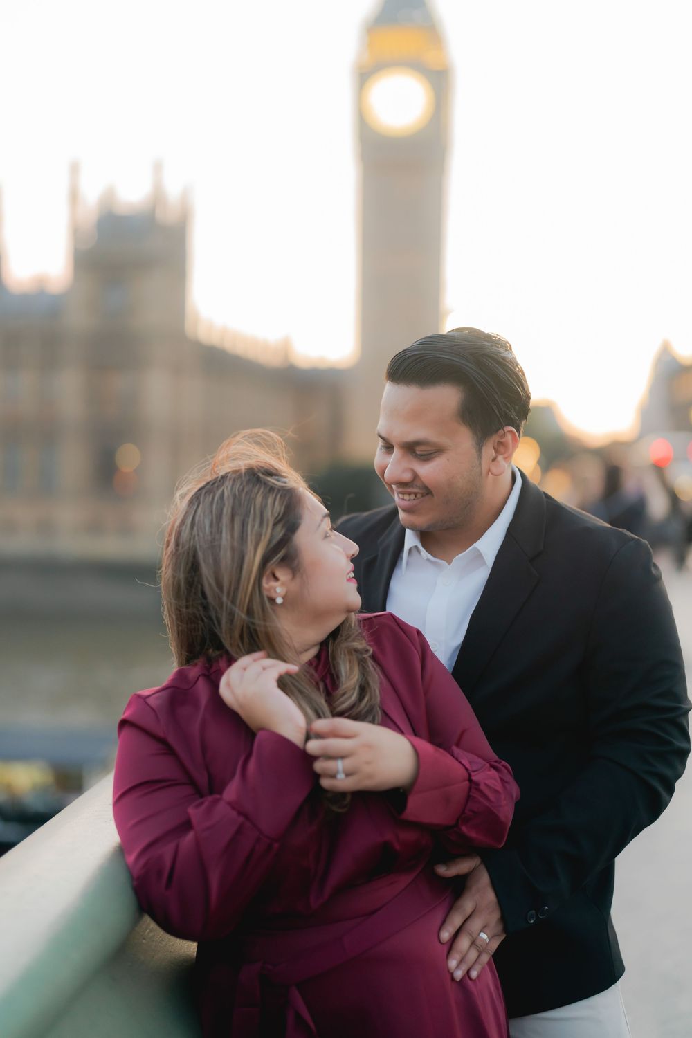 Couple embracing on Westminster Bridge with Big Ben and Houses of Parliament in background at golden hour.