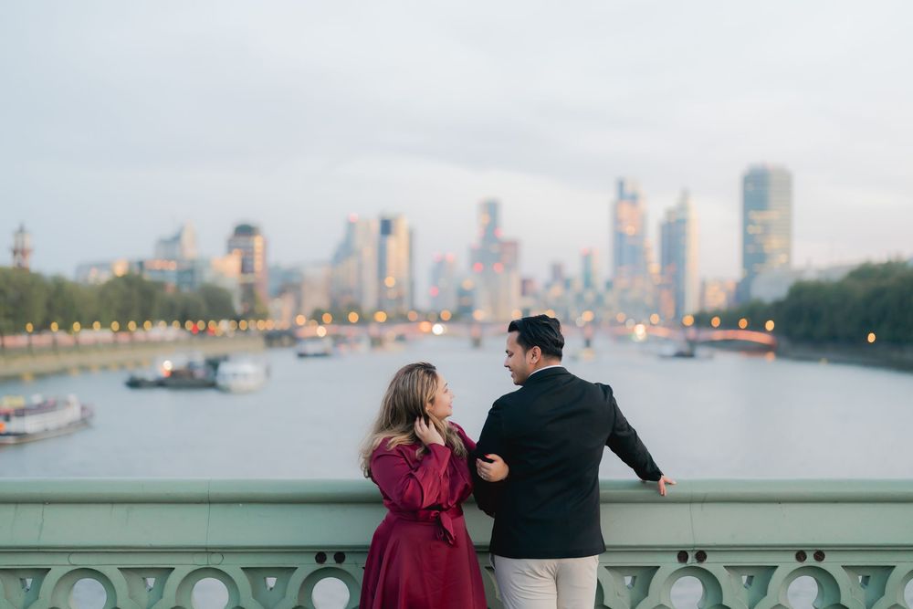 Couple sharing a romantic moment on Westminster Bridge with London skyline and River Thames at dusk.