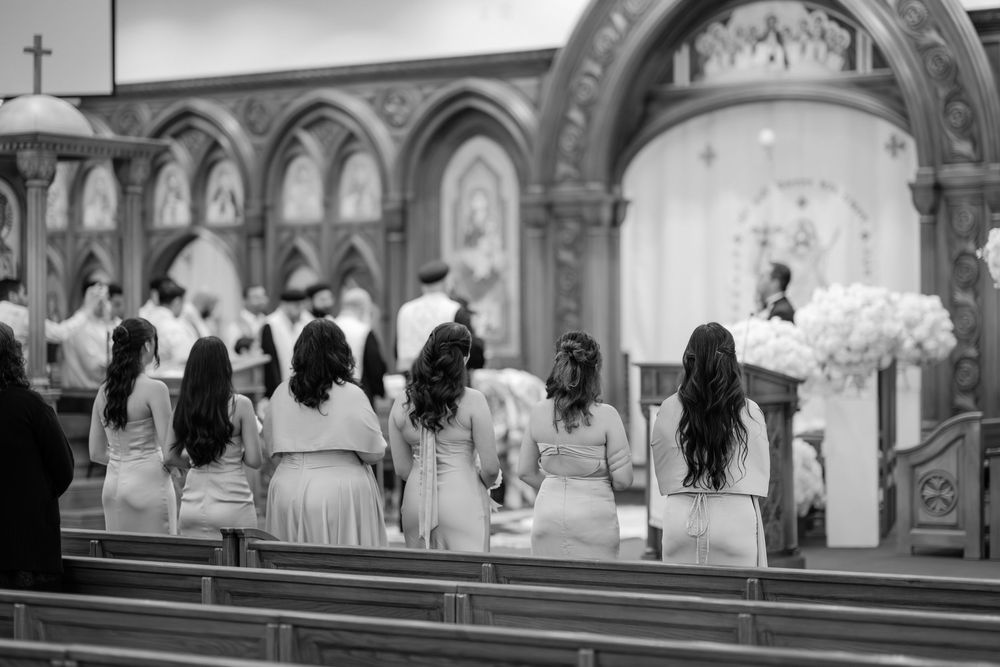 Bridesmaids in matching dresses stand at church pews during a wedding ceremony in a grand cathedral.