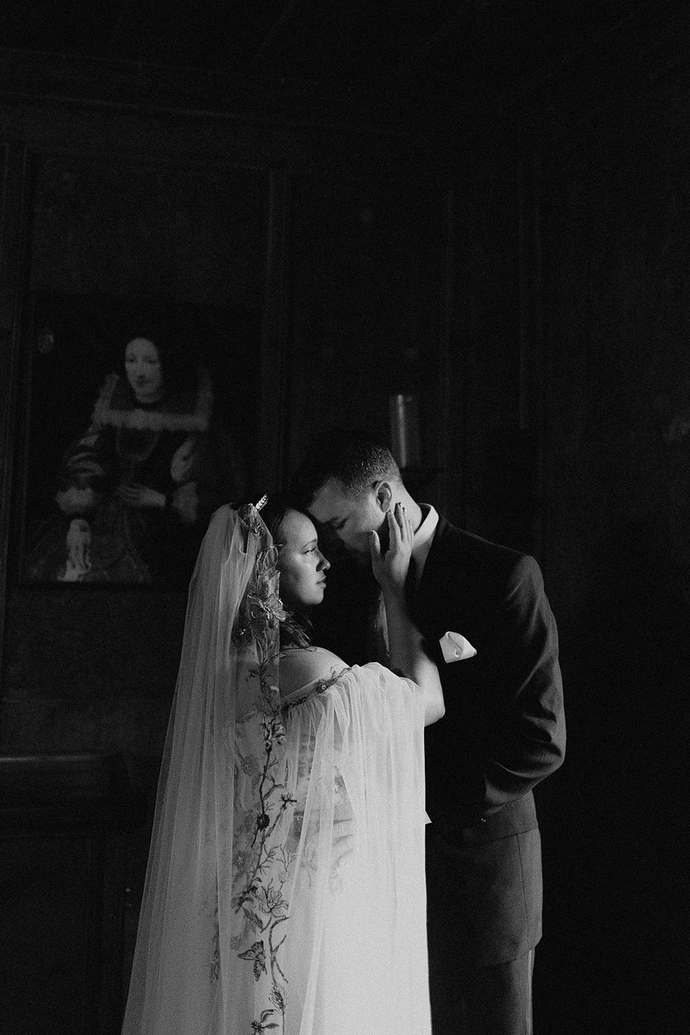 Black and white wedding photo of bride and groom sharing intimate moment before portrait painting.