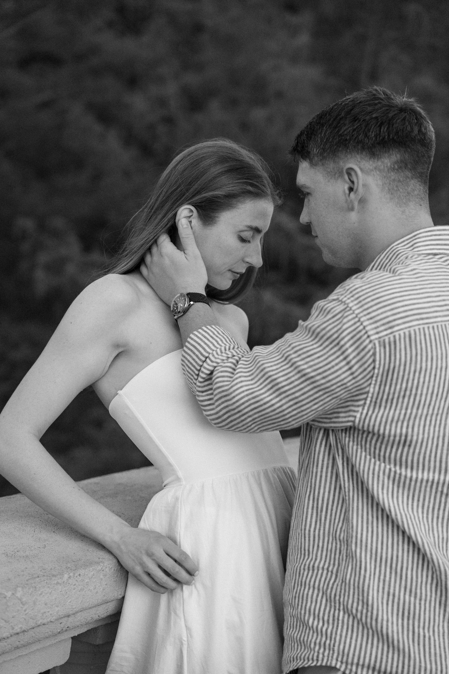 Black and white photo of a couple sharing an intimate moment on a balcony, man tenderly touching womans neck.