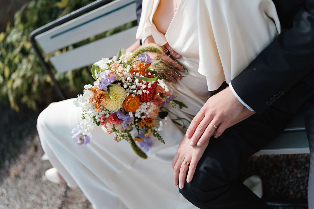 Bride and groom sitting on a bench holding a colorful wildflower wedding bouquet with roses and baby's breath.