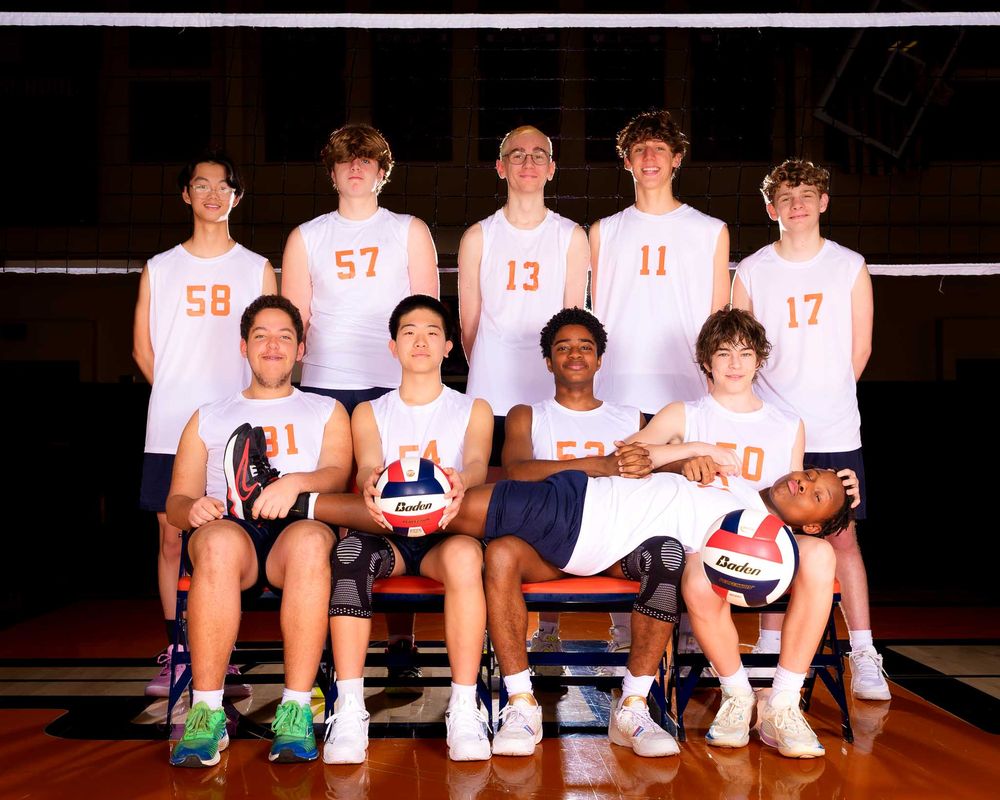 Hershey JV volleyball team in white jerseys poses for a group photo at the net by Deanna Fox, SportsFox Photography based in Hershey PA.
