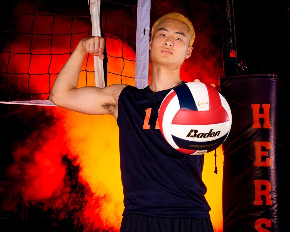 Hershey Trojan #11 holds volleyball at the net against an orange fog backdrop by Deanna Fox, SportsFox Photography based in Hershey PA.