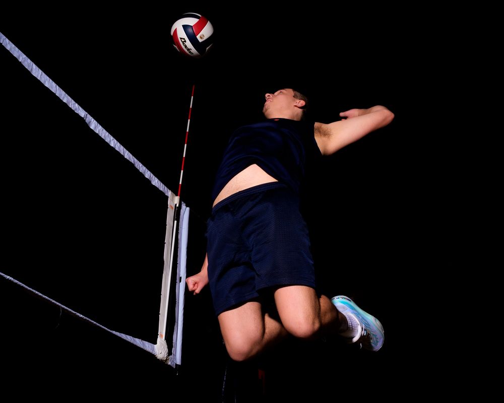 Low angle view of a Hershey Trojan player leaping to spike the ball over the net by Deanna Fox, SportsFox Photography based in Hershey PA.