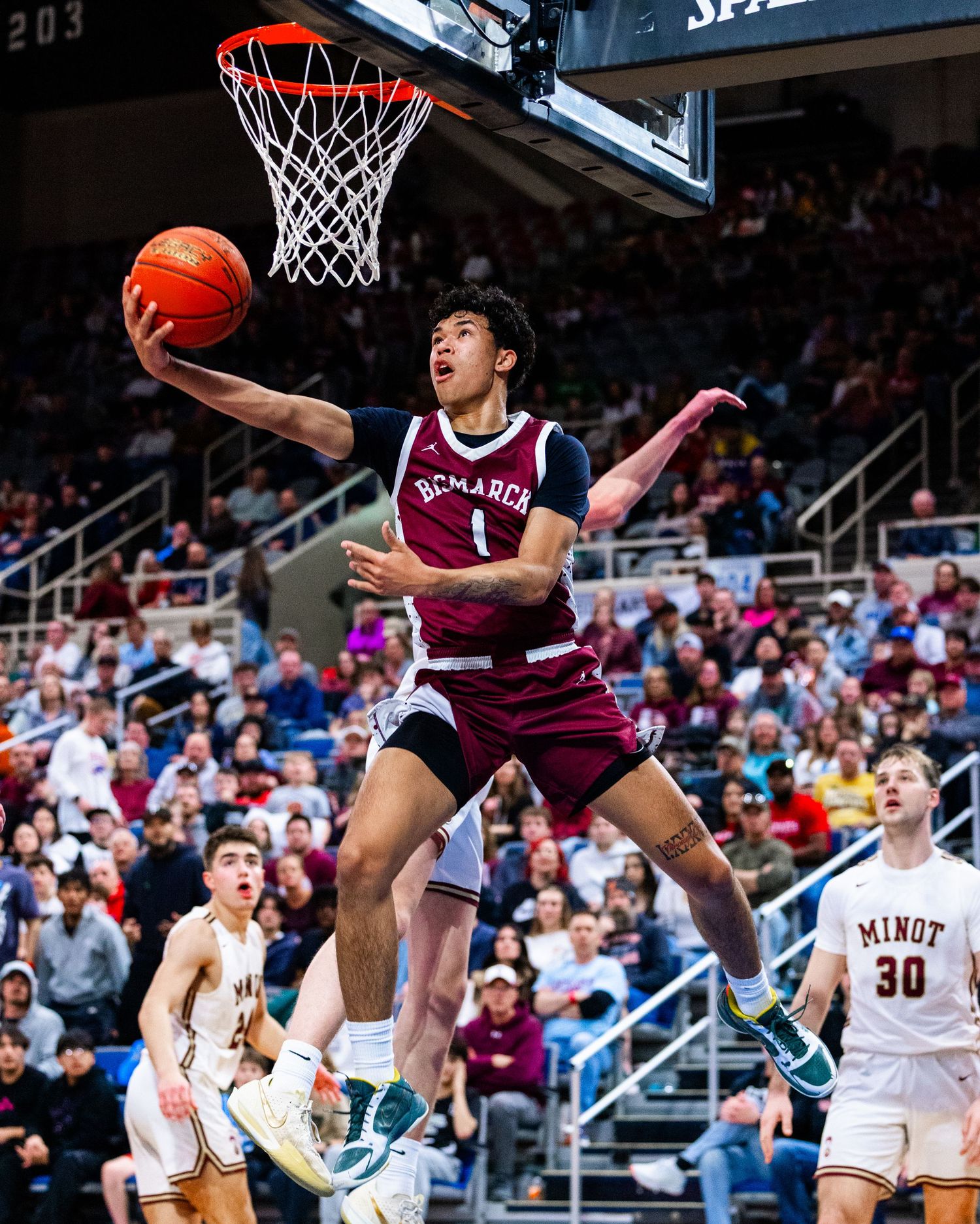 Basketball player in maroon uniform leaps high for a dramatic slam dunk attempt during an intense game.