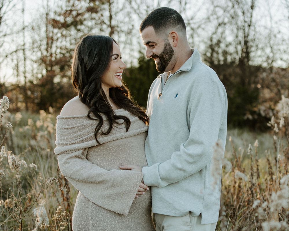 A couple shares an intimate moment in a field during golden hour while wearing neutral colored outfits.