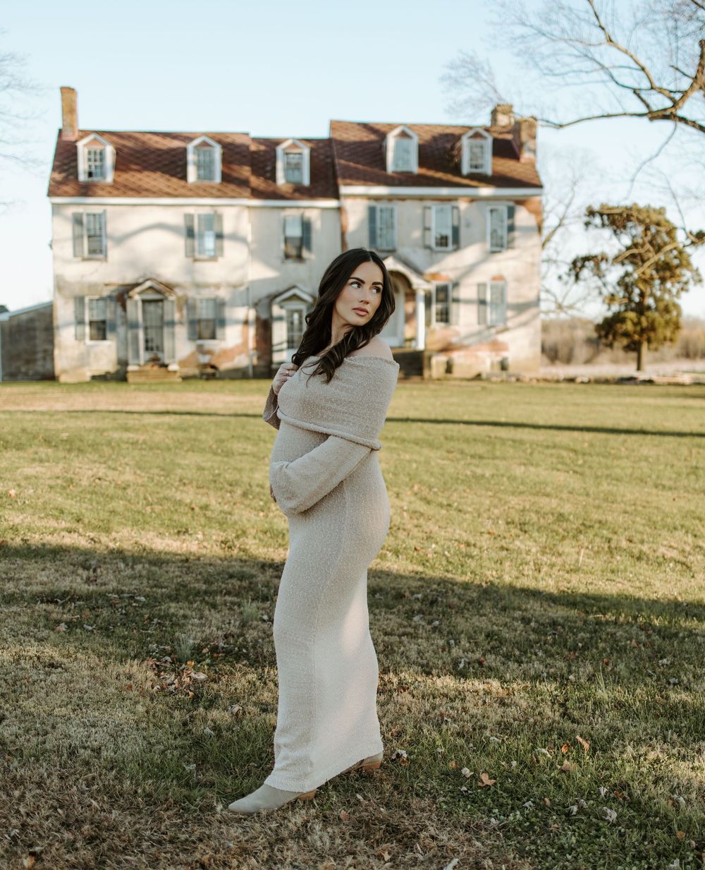 Pregnant woman in flowing dress poses in front of colonial style house.