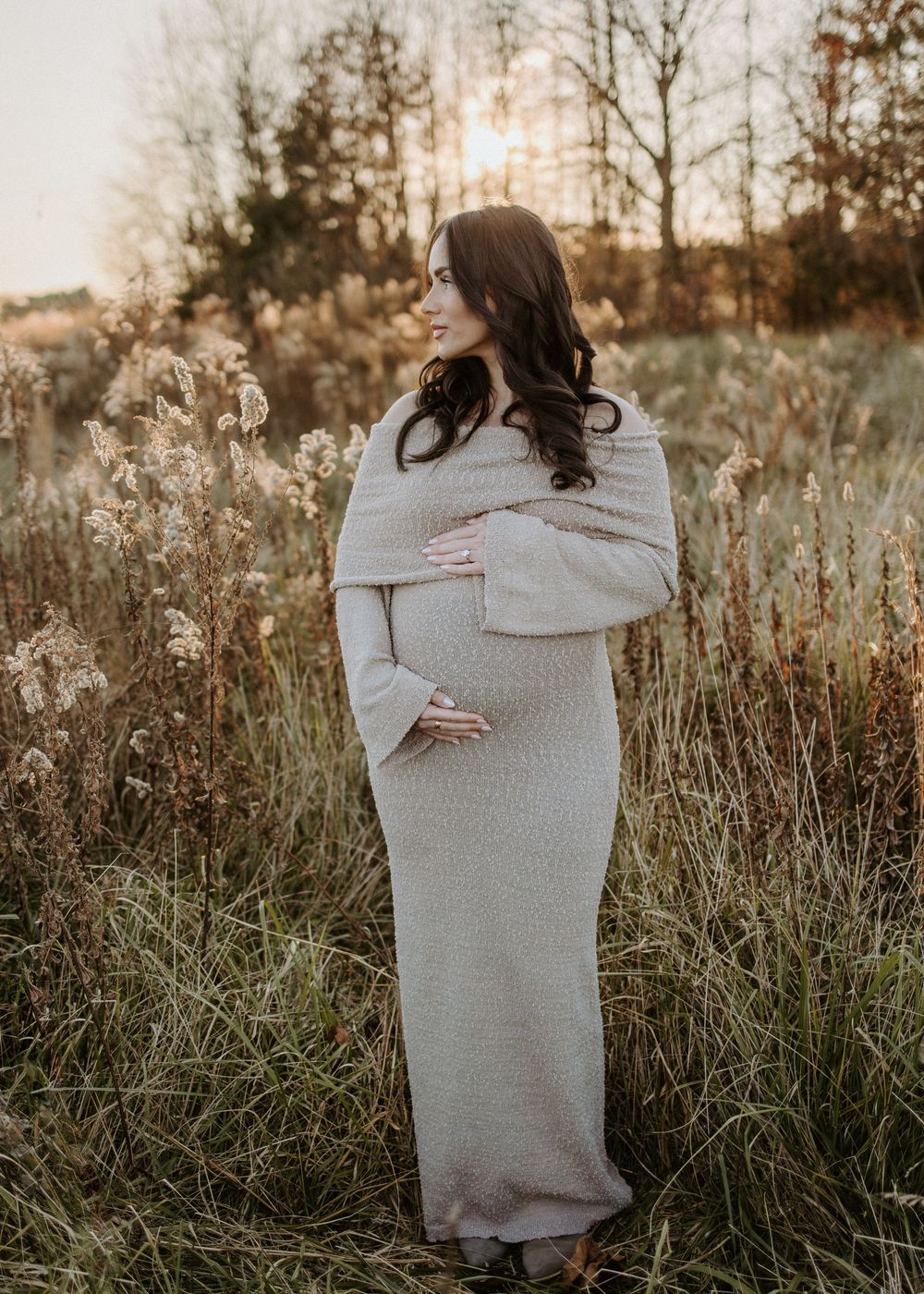 Side view of pregnant woman in cream dress standing in autumn field.